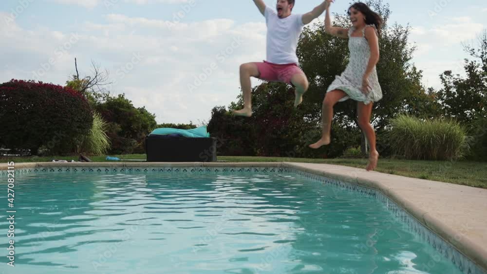 Young couple holding hands jump into swimming pool wearing clothes, Slow Motion
