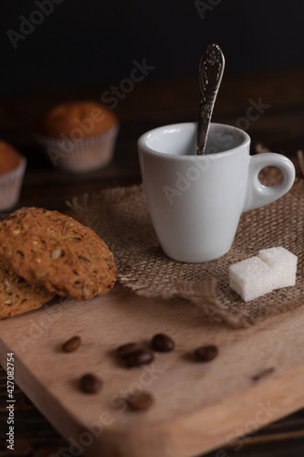 A cup of aromatic black coffee and coffee beans on a wooden table with cinnamon sticks and gingerbread. Coffee break. Coffee cup. 
