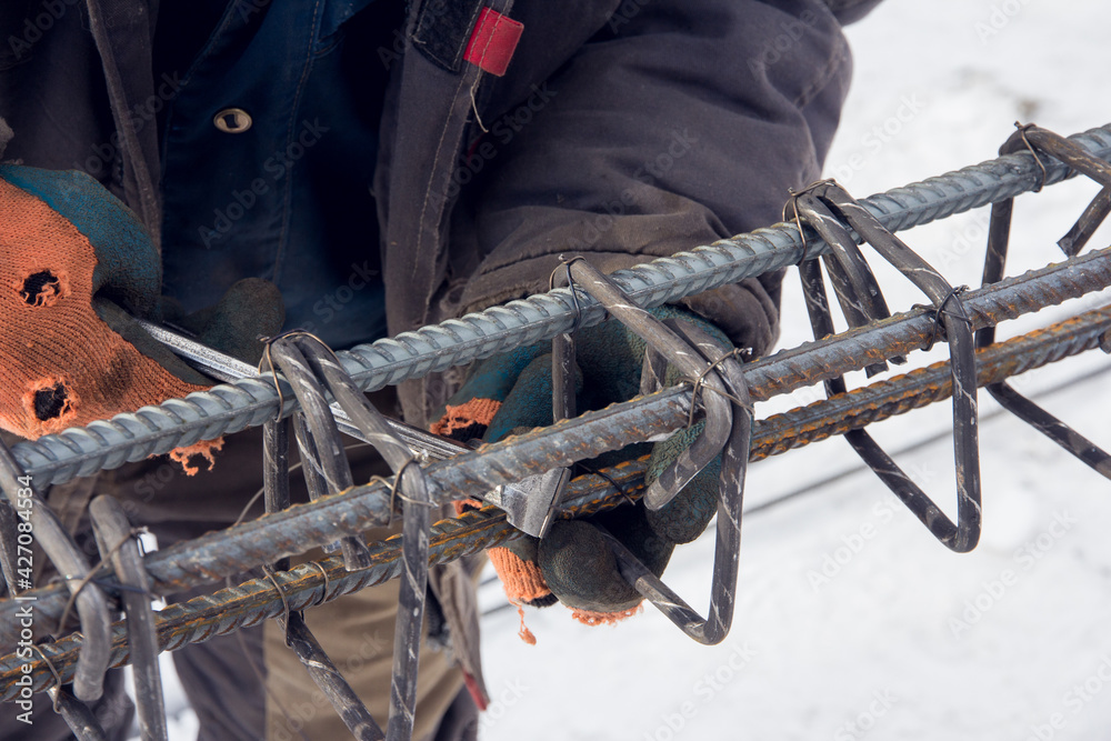 Concrete reinforcement. Tool at a construction site. The construction tool for monolithic works. Workers hands using steel wire and pincers to secure rebar