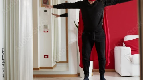 Man dressed as a superhero does gymnastics exercises at home.