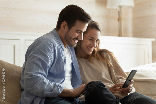 Smiling millennial couple rest at home use cellphone talk speak on video call online on gadget. Happy multiethnic man and woman have webcam digital virtual conference on smartphone device.