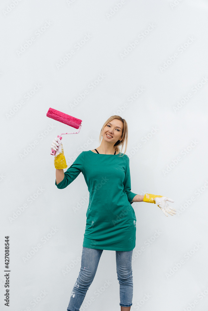A young girl poses with a pink roller before painting a white wall. Repair of the interior. A young girl poses with a pink roller before painting a white wall. Repair of the interior.