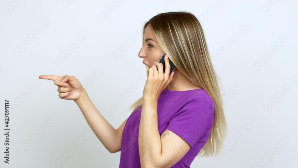 Young woman talking on mobile phone pointing to the side and presenting a product while smiling over isolated background Young woman talking on mobile phone pointing to the side and presenting a product while smiling over isolated background