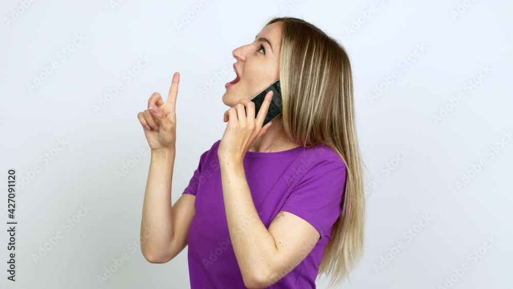 Young woman talking on mobile phone pointing a great idea and looking up over isolated background Young woman talking on mobile phone pointing a great idea and looking up over isolated background