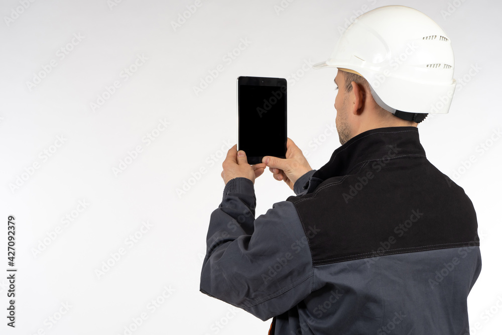 Worker takes photographs of something on phone. Man photographs something with a smartphone. Concept - he makes a photo report for the employer. Worker in a gray uniform. Man in a white safety helmet Worker takes photographs of something on phone. Man photographs something with a smartphone. Concept - he makes a photo report for the employer. Worker in a gray uniform. Man in a white safety helmet