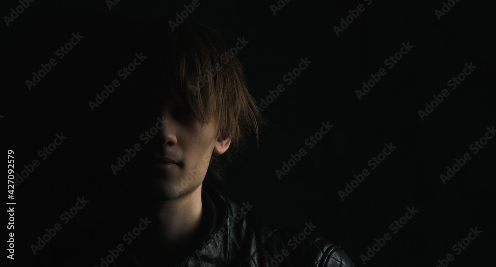 Portrait image of a young guy with long hair on a very dark background Portrait image of a young guy with long hair on a very dark background