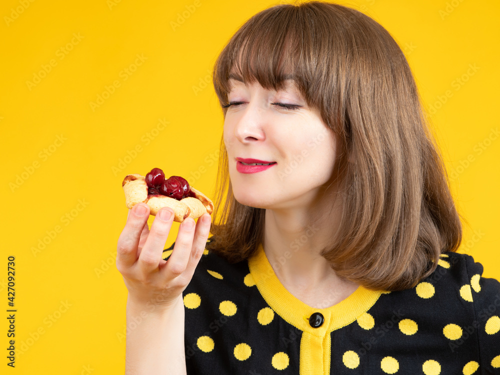 Woman eats cakes with berries. She bites cookie with delight. Girl holds a cake near her face. Young woman with a dissert in her hands. Concept - sale of dissertations. Dissert shop. Woman eats cakes with berries. She bites cookie with delight. Girl holds a cake near her face. Young woman with a dissert in her hands. Concept - sale of dissertations. Dissert shop.