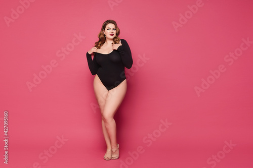Beautiful plump woman with full red lips wearing a black bodysuit against the pink background, studio shot with copy space