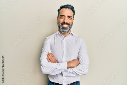 Middle age man with beard and grey hair wearing casual white shirt happy face smiling with crossed arms looking at the camera. positive person. © Krakenimages.com