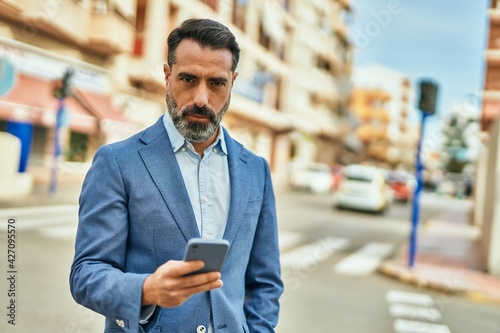 Middle age businessman with serious expression using smartphone at the city.