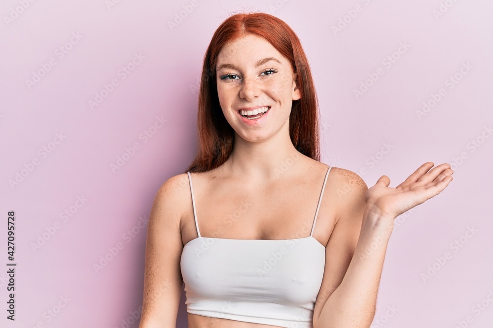 Young red head girl standing over pink background celebrating victory with happy smile and winner expression with raised hands Young red head girl standing over pink background celebrating victory with happy smile and winner expression with raised hands