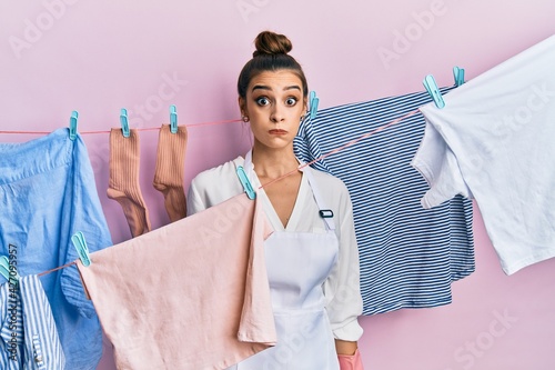 Beautiful brunette young woman washing clothes at clothesline puffing cheeks with funny face. mouth inflated with air, crazy expression.