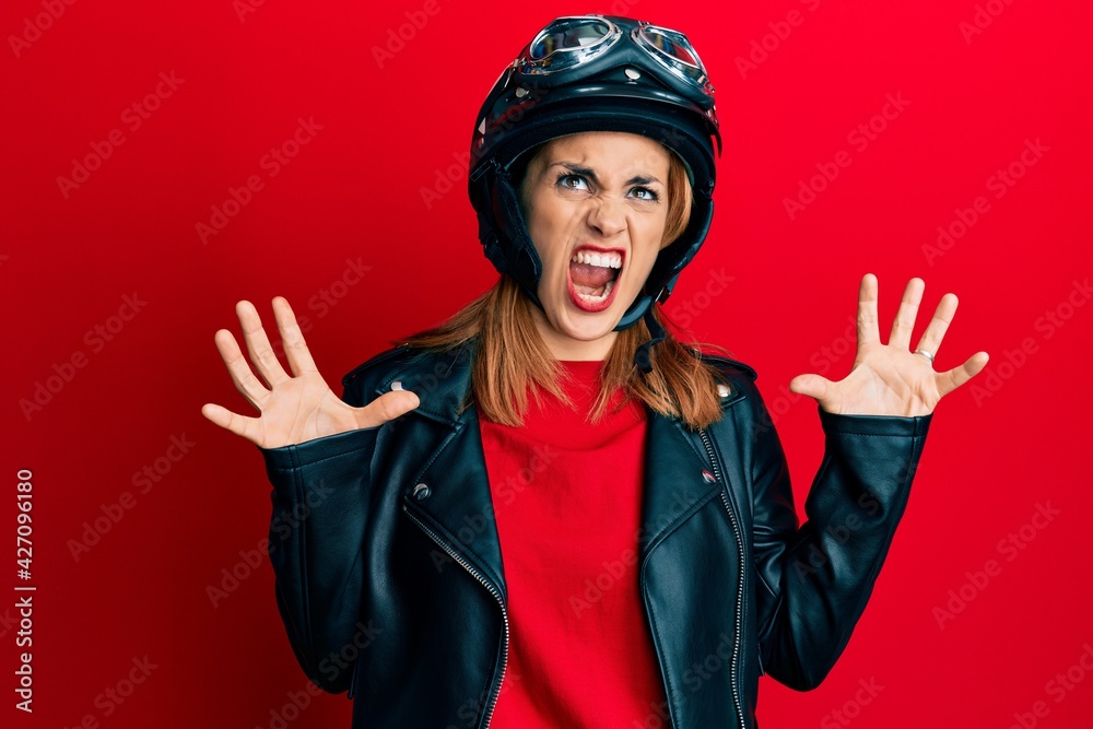 Hispanic young woman wearing motorcycle helmet crazy and mad shouting and yelling with aggressive expression and arms raised. frustration concept. Hispanic young woman wearing motorcycle helmet crazy and mad shouting and yelling with aggressive expression and arms raised. frustration concept.