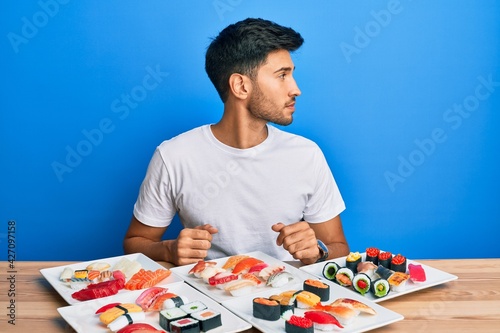Young handsome man eating sushi sitting on the table looking to side  relax profile pose with natural face with confident smile.