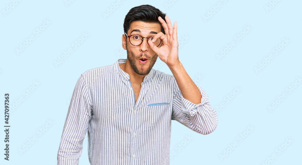 Young handsome man wearing casual clothes and glasses doing ok gesture shocked with surprised face, eye looking through fingers. unbelieving expression. Young handsome man wearing casual clothes and glasses doing ok gesture shocked with surprised face, eye looking through fingers. unbelieving expression.