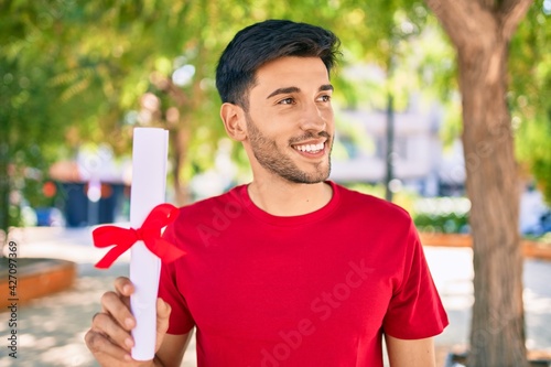 Young latin man smiling happy holding graduated diploma standing at the city. photo