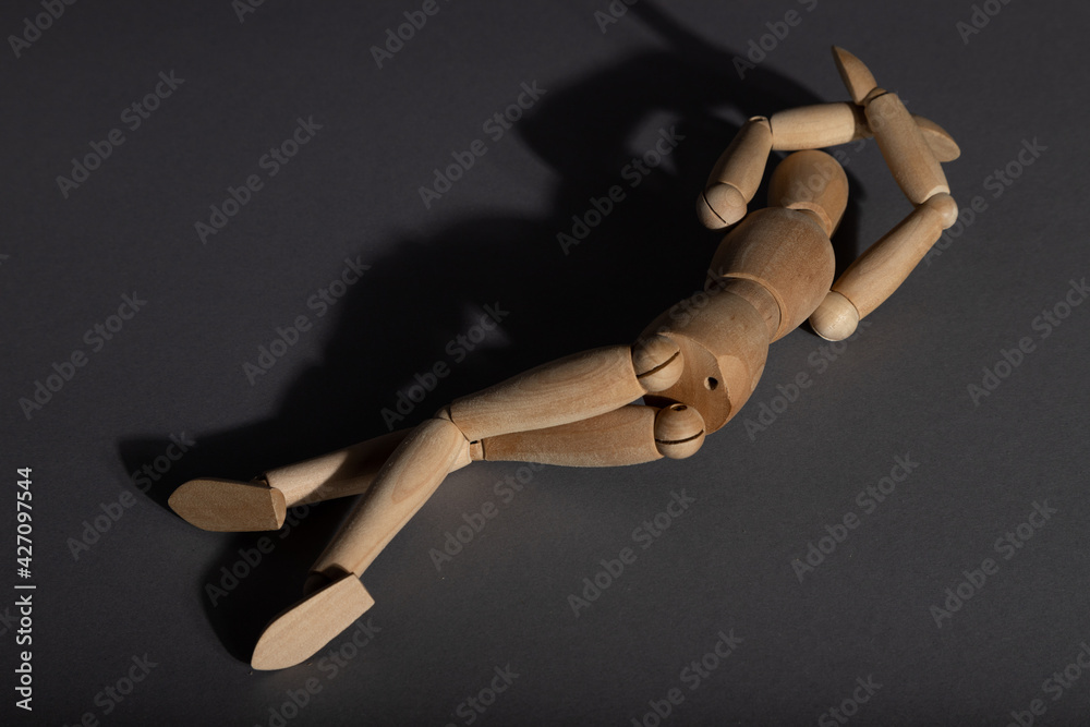 Wooden mannequin lies in a protective position on gray background. violence, depression disorder concept. copy space. Wooden mannequin lies in a protective position on gray background. violence, depression disorder concept. copy space.