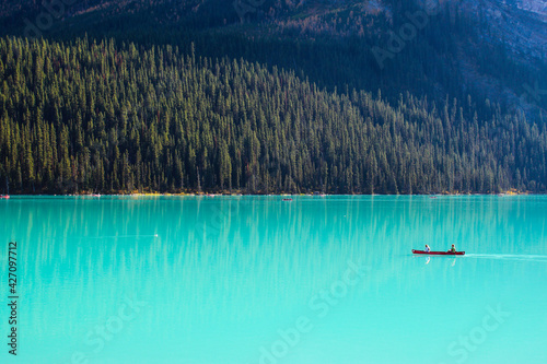 Solo canoe in empty turqouise blue glacial lake surrounded by natural wilderness forest and mountain