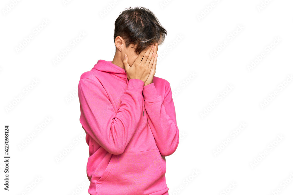 Young hispanic man wearing casual pink sweatshirt with sad expression covering face with hands while crying. depression concept.
