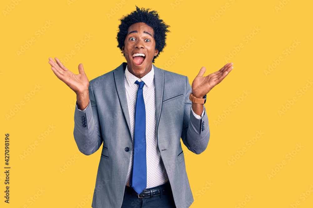 Handsome african american man with afro hair wearing business jacket celebrating crazy and amazed for success with arms raised and open eyes screaming excited. winner concept Handsome african american man with afro hair wearing business jacket celebrating crazy and amazed for success with arms raised and open eyes screaming excited. winner concept