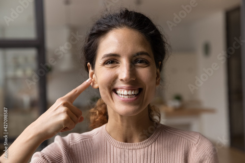 Εκτύπωση καμβά Portrait of smiling hispanic lady look at camera point finger on face show smooth silky fresh clear skin after using self care cosmetic