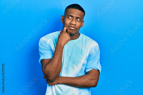 Young black man wearing tye die t shirt serious face thinking about question with hand on chin, thoughtful about confusing idea