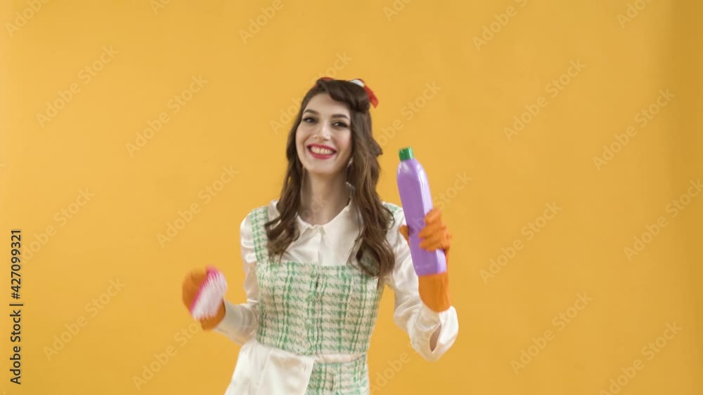 A young woman dances with a brush and household chemicals in her hands. Pin-up style. Cleaning concept. Wavy hair. A young woman dances with a brush and household chemicals in her hands. Pin-up style. Cleaning concept. Wavy hair.