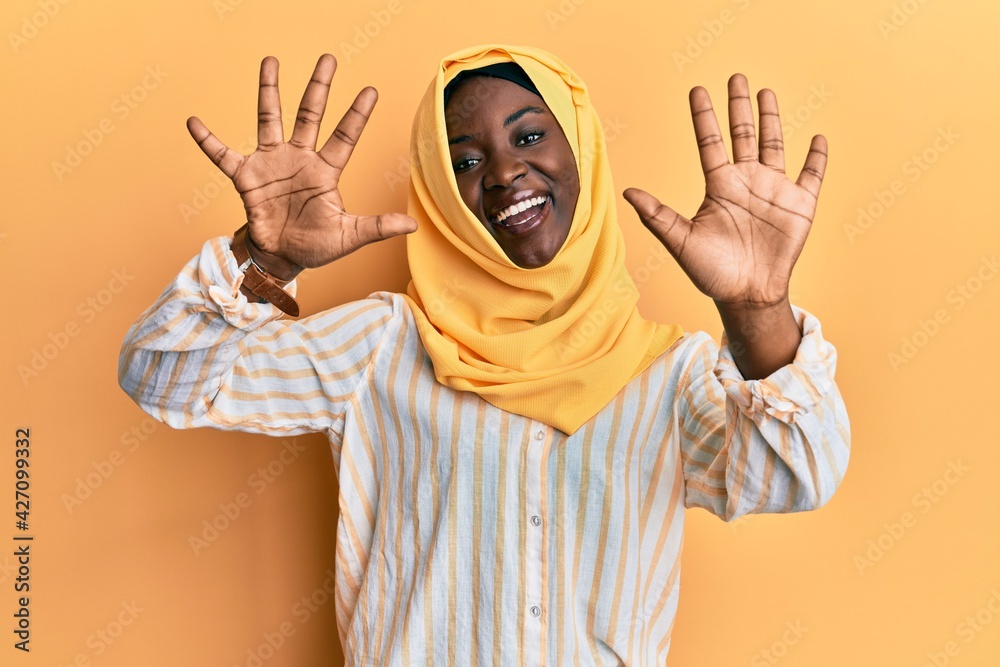 Beautiful african young woman wearing traditional islamic hijab scarf showing and pointing up with fingers number ten while smiling confident and happy.