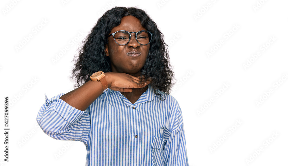 Beautiful african young woman wearing casual clothes and glasses cutting throat with hand as knife, threaten aggression with furious violence Beautiful african young woman wearing casual clothes and glasses cutting throat with hand as knife, threaten aggression with furious violence