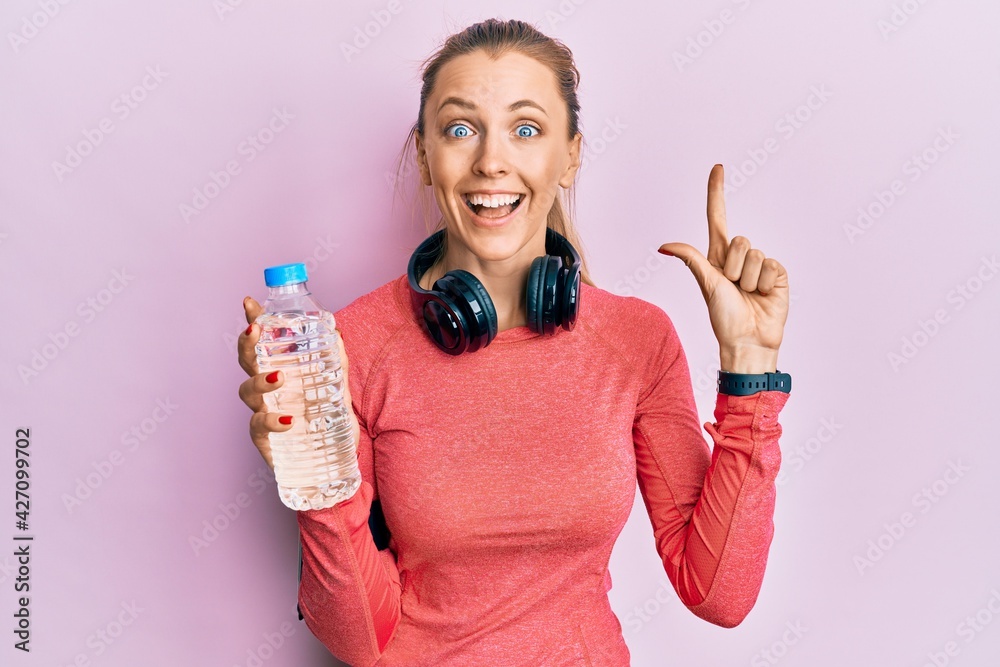 Beautiful caucasian sports woman wearing sportswear drinking bottle of water smiling with an idea or question pointing finger with happy face, number one Beautiful caucasian sports woman wearing sportswear drinking bottle of water smiling with an idea or question pointing finger with happy face, number one