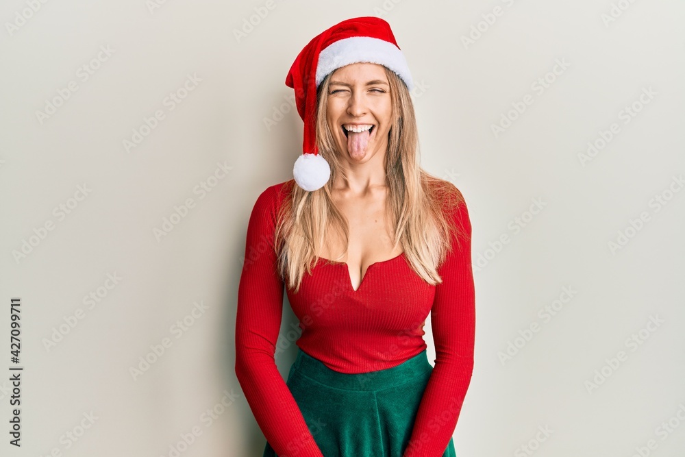 Beautiful caucasian woman wearing christmas costume and hat sticking tongue out happy with funny expression. emotion concept.