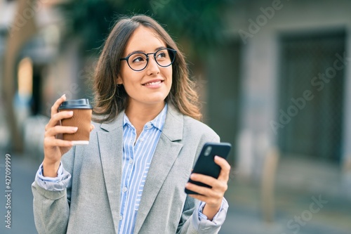 Young hispanic businesswoman using smartphone and drinking take away coffee at the city.