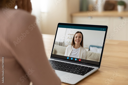 Two young women good friends sisters colleagues have fun chat by video call enjoy pleasant internet conversation via e conference app. Rear view of female teacher talk to student using laptop webcam
