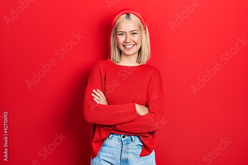 Beautiful blonde woman wearing casual red sweater happy face smiling with crossed arms looking at the camera. positive person.