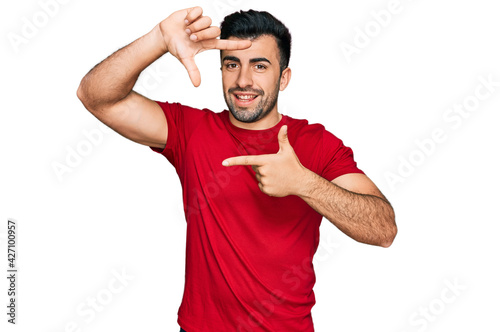 Hispanic man with beard wearing casual red t shirt smiling making frame with hands and fingers with happy face. creativity and photography concept.