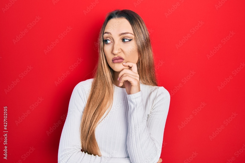 Young blonde girl wearing casual clothes serious face thinking about question with hand on chin, thoughtful about confusing idea Young blonde girl wearing casual clothes serious face thinking about question with hand on chin, thoughtful about confusing idea