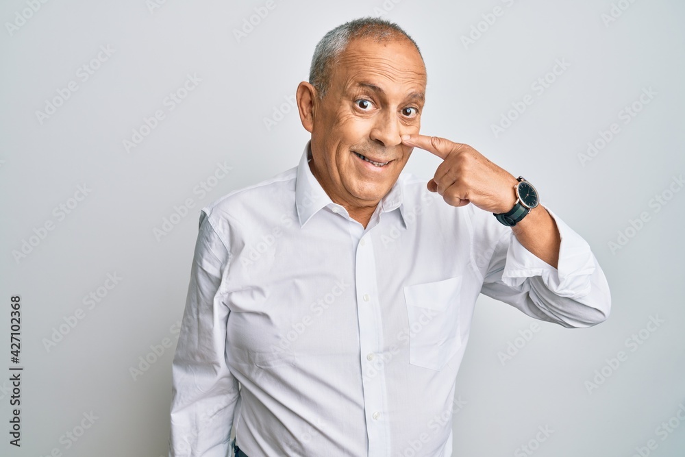 Handsome senior man wearing casual white shirt pointing with hand finger to face and nose, smiling cheerful. beauty concept Handsome senior man wearing casual white shirt pointing with hand finger to face and nose, smiling cheerful. beauty concept