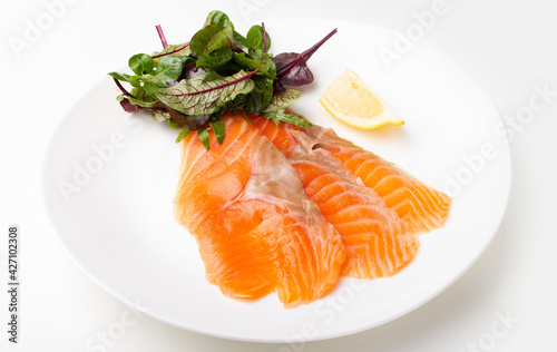 Salmon pieces on a white plate with basil leaves and lemon wedge 
