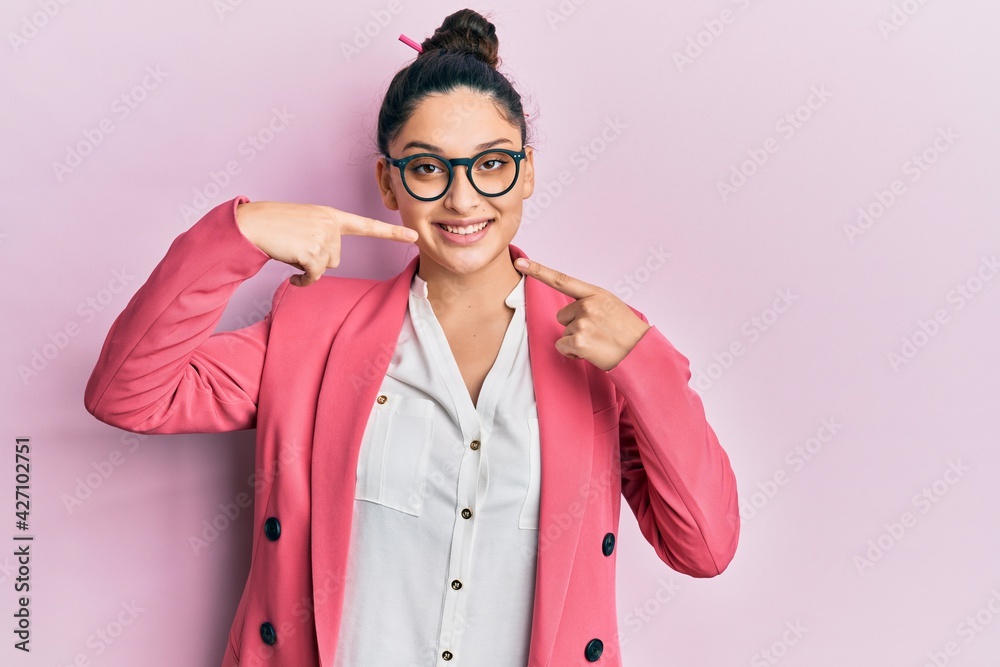 Beautiful middle eastern woman wearing business jacket and glasses smiling cheerful showing and pointing with fingers teeth and mouth. dental health concept. Beautiful middle eastern woman wearing business jacket and glasses smiling cheerful showing and pointing with fingers teeth and mouth. dental health concept.