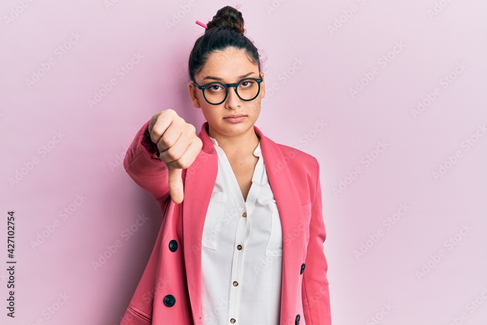 Beautiful middle eastern woman wearing business jacket and glasses looking unhappy and angry showing rejection and negative with thumbs down gesture. bad expression. Beautiful middle eastern woman wearing business jacket and glasses looking unhappy and angry showing rejection and negative with thumbs down gesture. bad expression.