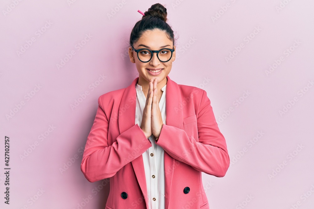 Beautiful middle eastern woman wearing business jacket and glasses praying with hands together asking for forgiveness smiling confident.