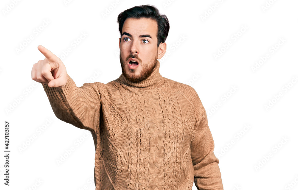 Young hispanic man wearing casual clothes pointing with finger surprised ahead, open mouth amazed expression, something on the front Young hispanic man wearing casual clothes pointing with finger surprised ahead, open mouth amazed expression, something on the front