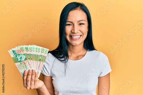 Beautiful hispanic woman holding hong kong 50 dollars banknotes looking positive and happy standing and smiling with a confident smile showing teeth