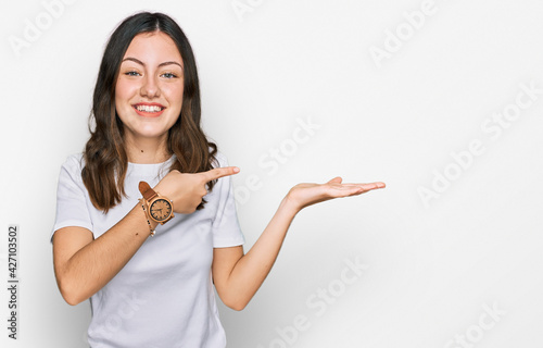 Young beautiful woman wearing casual white t shirt amazed and smiling to the camera while presenting with hand and pointing with finger.