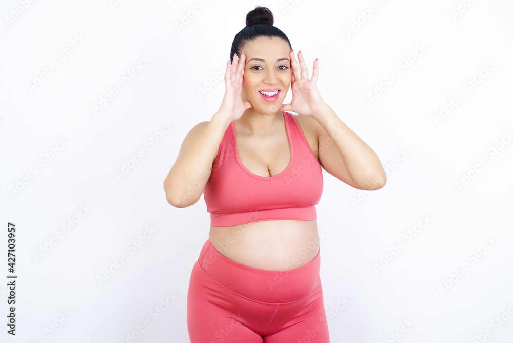young beautiful Arab pregnant woman in sports clothes against white wall Pleasant looking cheerful, Happy reaction young beautiful Arab pregnant woman in sports clothes against white wall Pleasant looking cheerful, Happy reaction