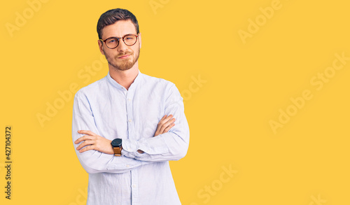 Handsome young man with bear wearing elegant business shirt and glasses skeptic and nervous, disapproving expression on face with crossed arms. negative person.