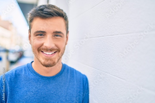 Young caucasian man smiling happy leaning on the wall at the city.