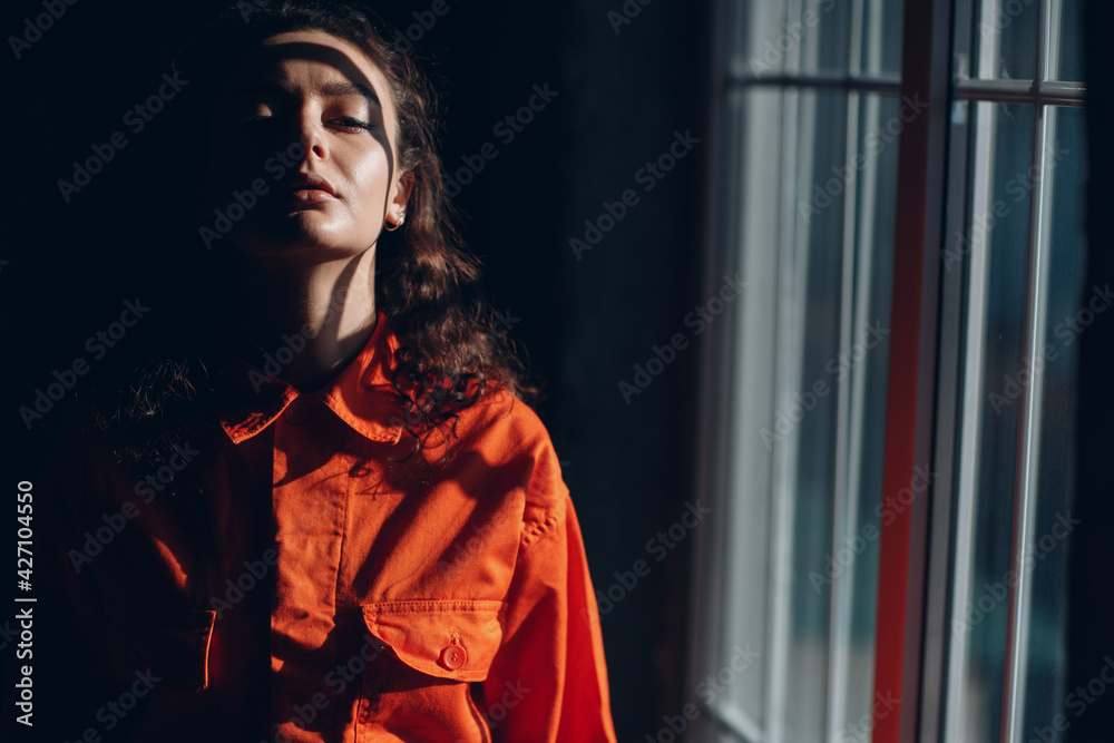 Young brunette curly woman in orange suit. Female in colorful overalls portrait.