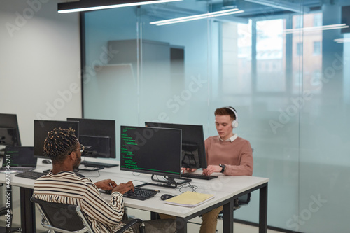 Background image of IT programmers or students using computers in office interior with glass wall, copy space
