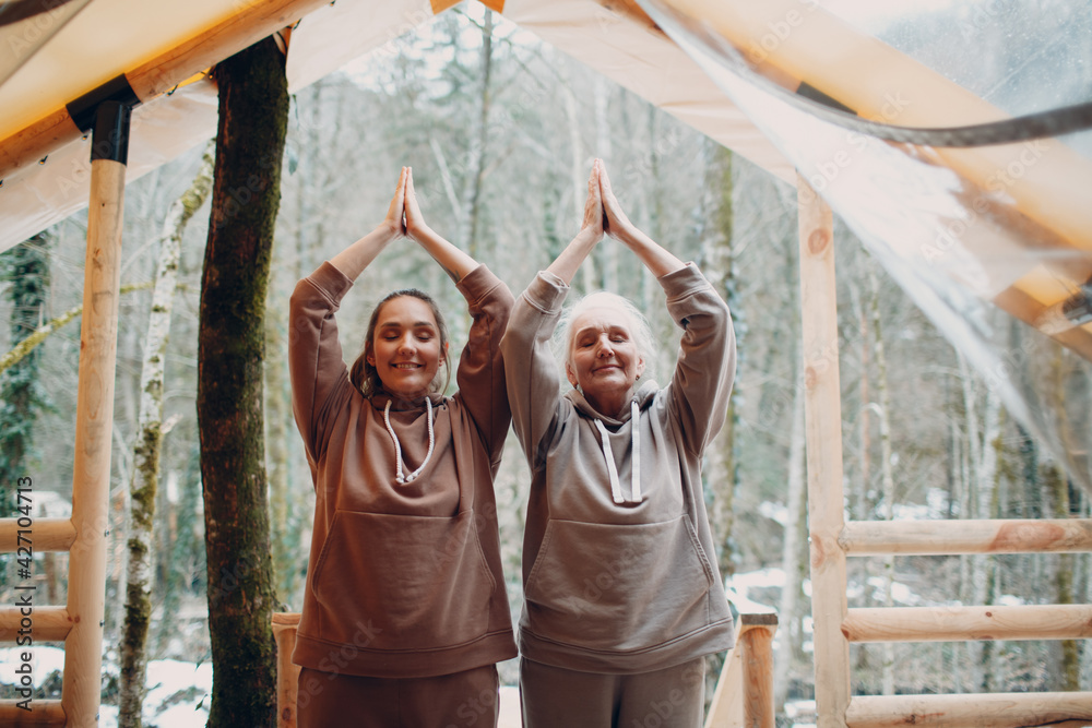 Woman senior and young relaxing at glamping camping tent outdoor. Women family elderly mother and young daughter doing yoga and meditation indoor. Modern zen-like vacation lifestyle concept.